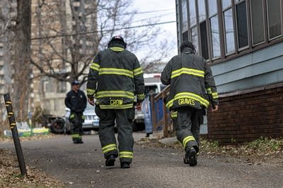 Two firefighters walk together, seen from behind.