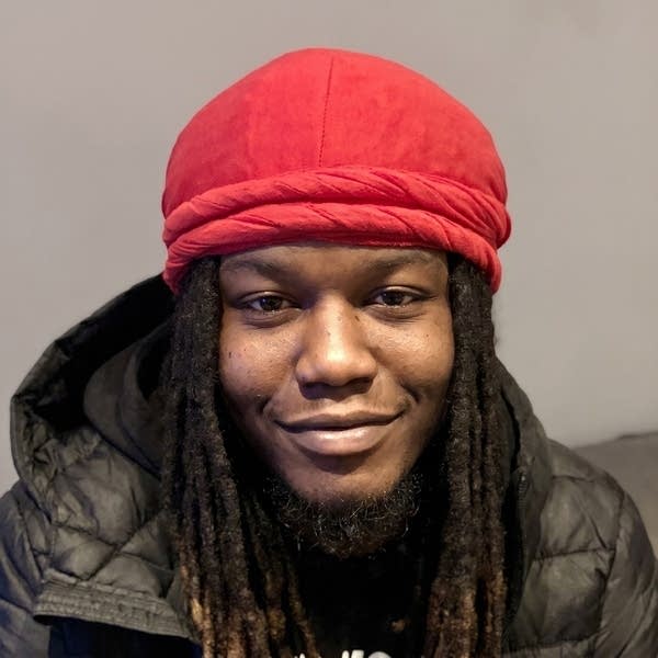 A man in a black coat and red hat smiles for a photo.
