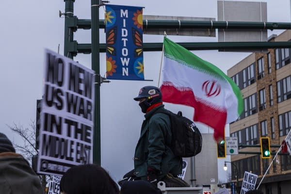 A protester stands above a crowd holding an Iranian flag.