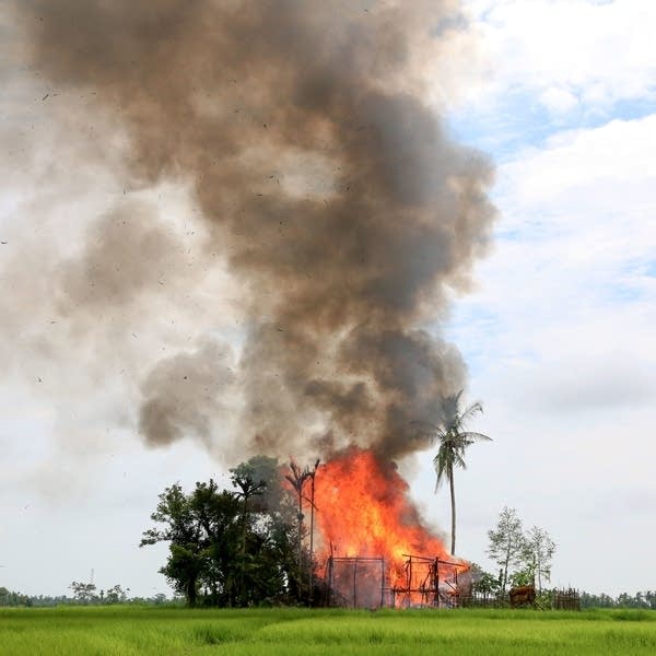 A house in Rakhine state is consumed by flames, as journalists look on.