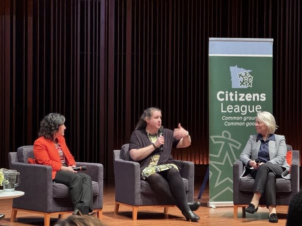 three women talk while sitting on a stage with a citizens league banner behind them