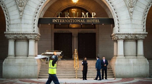 A construction worker carries away trash as security staff patrol outside the Trump International Hotel in Washington, D.C. during the hotel's opening in 2016.