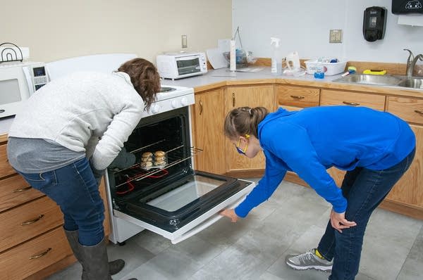 Two people open an oven door. 