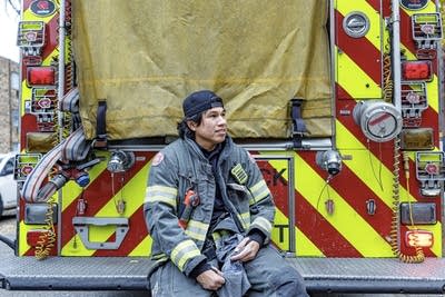 A firefighter sits on the bumper of a fire engine.