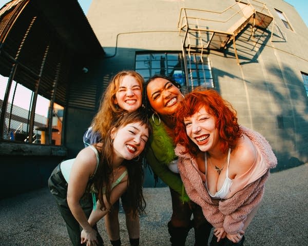 Four musicians smile for a portrait while standing outside a venue