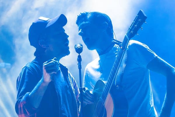 Two people singing into one microphone on stage