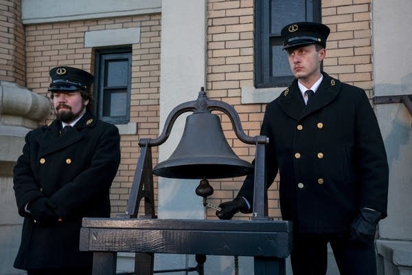 Two men dressed as lighthouse keepers ring a metal bell.
