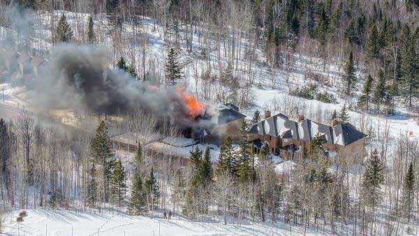 Aerial shot of a ski lodge on fire in the woods.