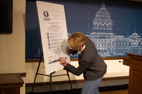 A candidate leans down to sign a cardboard poster.