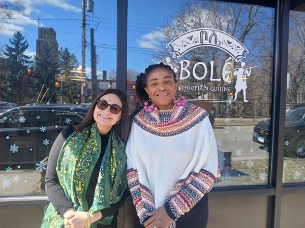 Two people pose in front of a restaurant