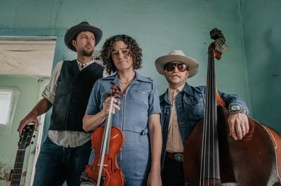 Three people standing in an abandoned house, holding instruments