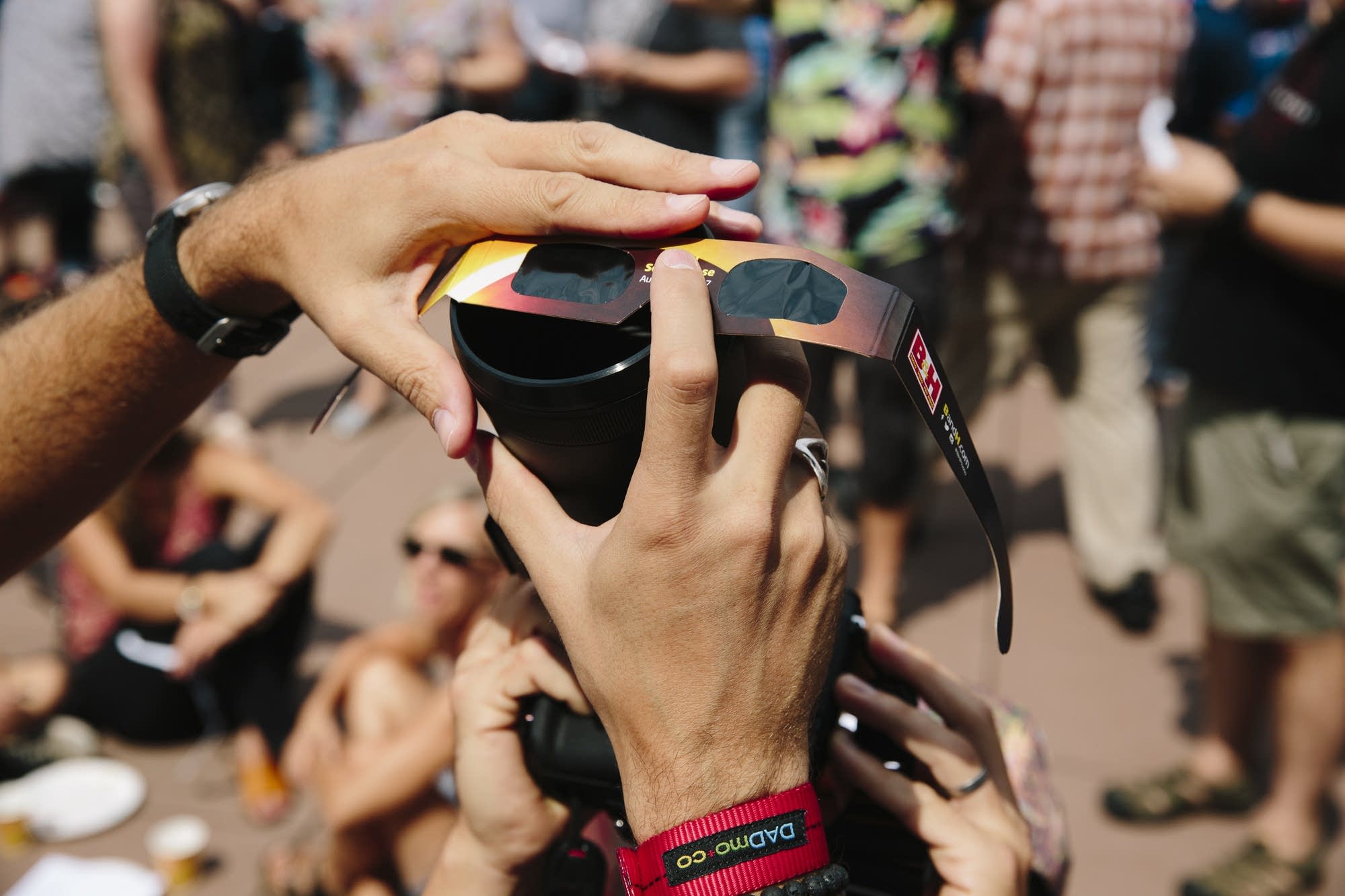 People hold eclipse glasses in front of a camera.