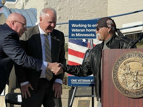 Three people smile, while two of them shake hands.