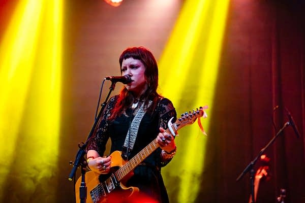 A musician sings and plays guitar onstage in a music venue