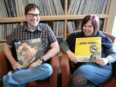 Two people sitting in chairs and holding vinyl albums