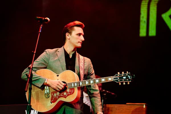 A musician plays guitar on an outdoor stage
