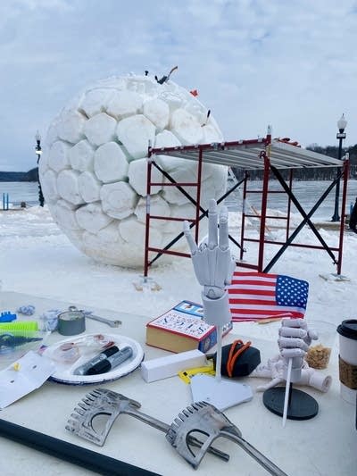 Posable hands sit on a table for reference in front of a snow sculpture in progress.