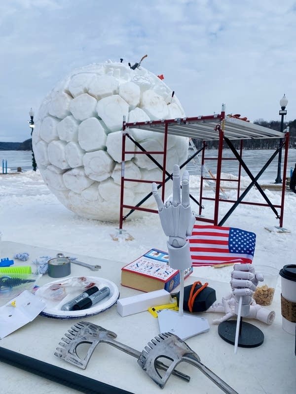 Posable hands sit on a table for reference in front of a snow sculpture in progress.