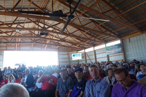 A large crowd sits in chairs inside a large barn.