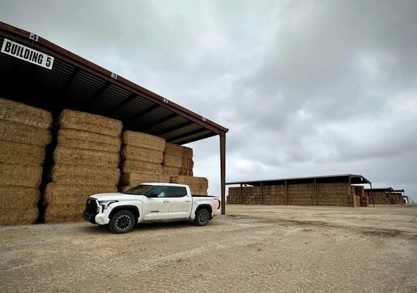 A truck parks near some hay bale storage.