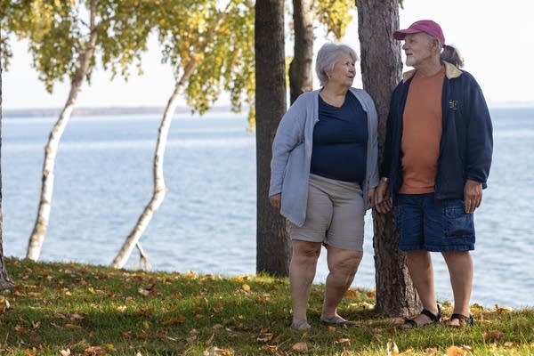 A couple stands on the shore of a lake.