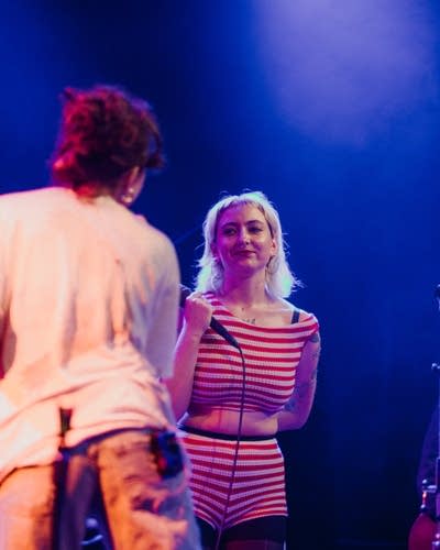 Two women sing into microphones on a lighted stage.