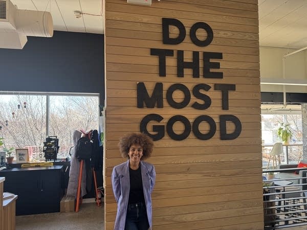 A woman stands near a sign that reads "Do The Most Good."