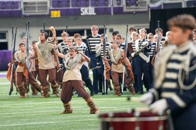 A marching band performs on the field of a football stadium.