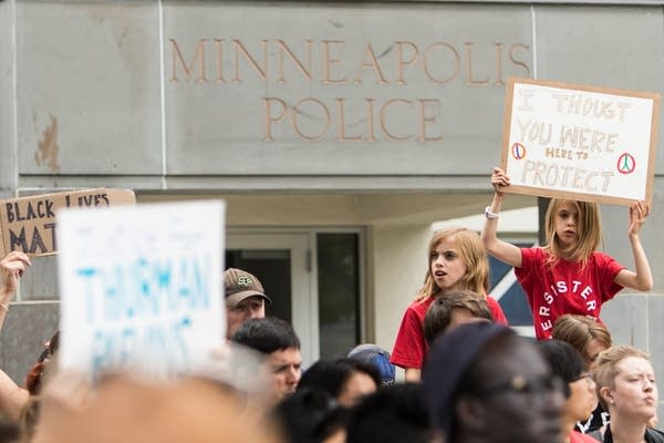 A young girl holds a sign that reads "I thought you were here to protect."