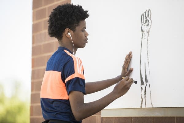 Young person paints a mural on a brick wall.