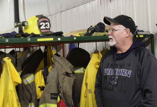 A man standing beside lockers with firefighter helmets and jackets. 