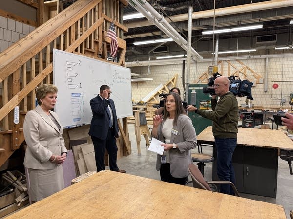 A group of politicians and reporters tour a university wood shop.