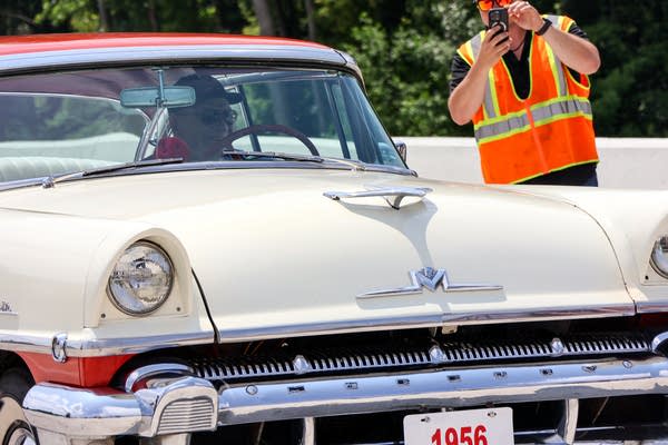 A man is seen behind the wheel of a white classic car.