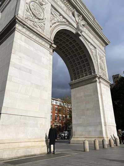 Wide shot of a man standing next to the Washington Square Arch in New York City.