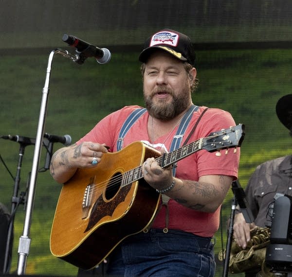 A man sings and plays guitar on a large outdoor stage
