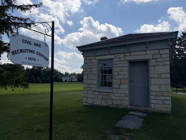 A small, limestone building sits in a grass field.