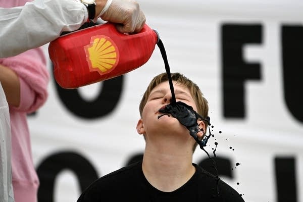Climate activists pour a black liquid to represent oil into the mouth of a fellow activist as they demonstrate against oil giant Shell on the beach in St. Ives in Cornwall, England, on June 11, 2021.