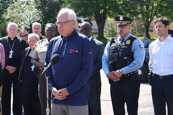 Minn. Gov. Tim Walz stands in front of church and political leaders at an outdoor press conference.