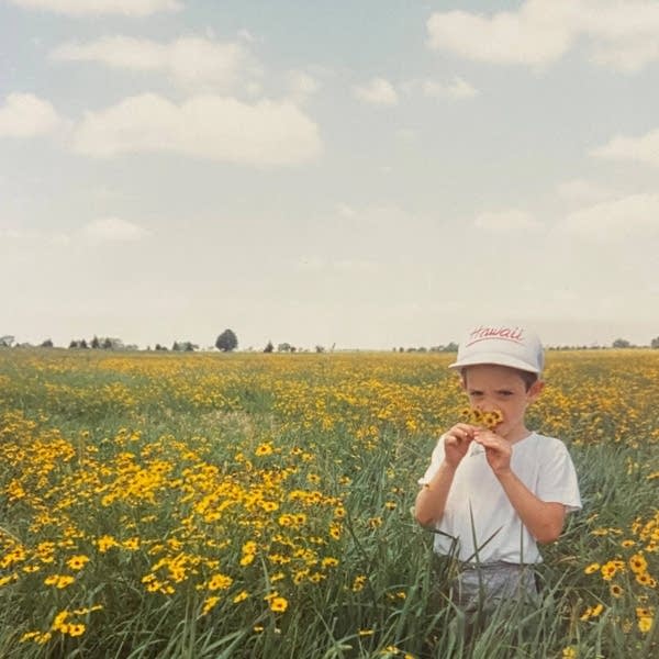 A little boy stands in a vast field of wildflowers, holding several flowers to his nose