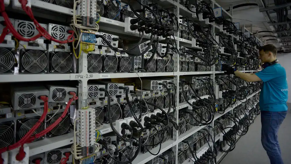 Technician servicing rows of cryptocurrency mining equipment at a mining facility in Russia