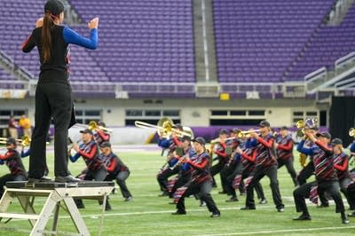 A marching band performs on the field of a football stadium.