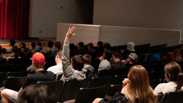 A high school audience member raises their hand in an auditorium at a Class Notes concert