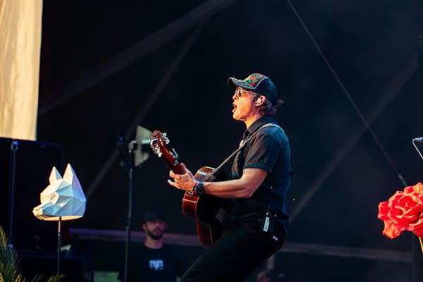 A musician sings and plays guitar on an outdoor stage