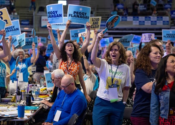 A crowd of attendees cheer from the convention floor while holding signs.