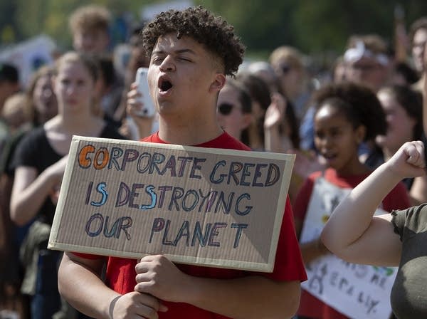 A teen holds a sign that reads "Corporate green is destroying our planet."