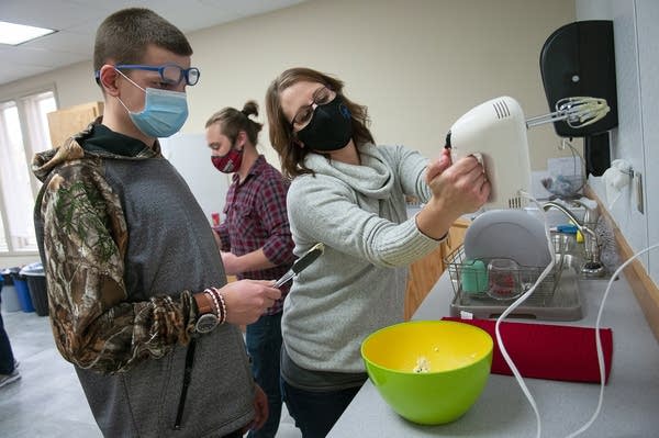 A woman holds up a hand mixer while talking with a young man. 