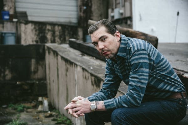 A man in fashionable clothes sits at the edge of a loading dock