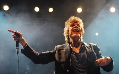 A man smiles and gestures while performing onstage