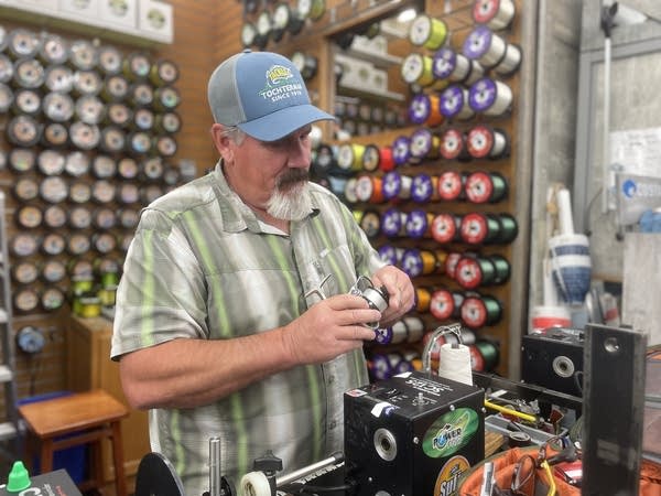 A man with a blue baseball cap and colorful shirt winds fishing line at a tackle store in Baltimore. 