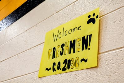 A yellow sign hanging on a concrete wall reads, "Welcome freshmen! C.O. 2030."